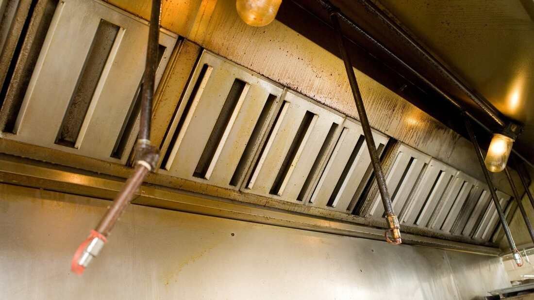 Commercial kitchen exhaust hood with angled metal baffles and fire suppression nozzles.