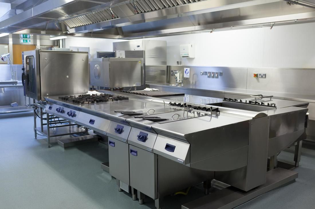 Stainless steel commercial kitchen with cooking range and ventilation system.