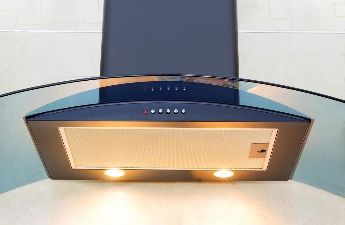 Black kitchen range hood with glass visor and two lights, mounted on a wall.