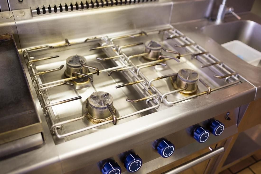 Stainless steel commercial stovetop with four burners and blue knobs.