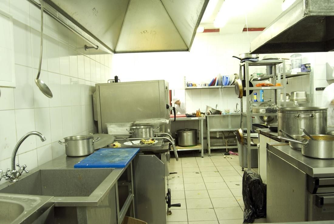 Commercial kitchen with stainless steel appliances, pots, and sinks; cooking area.