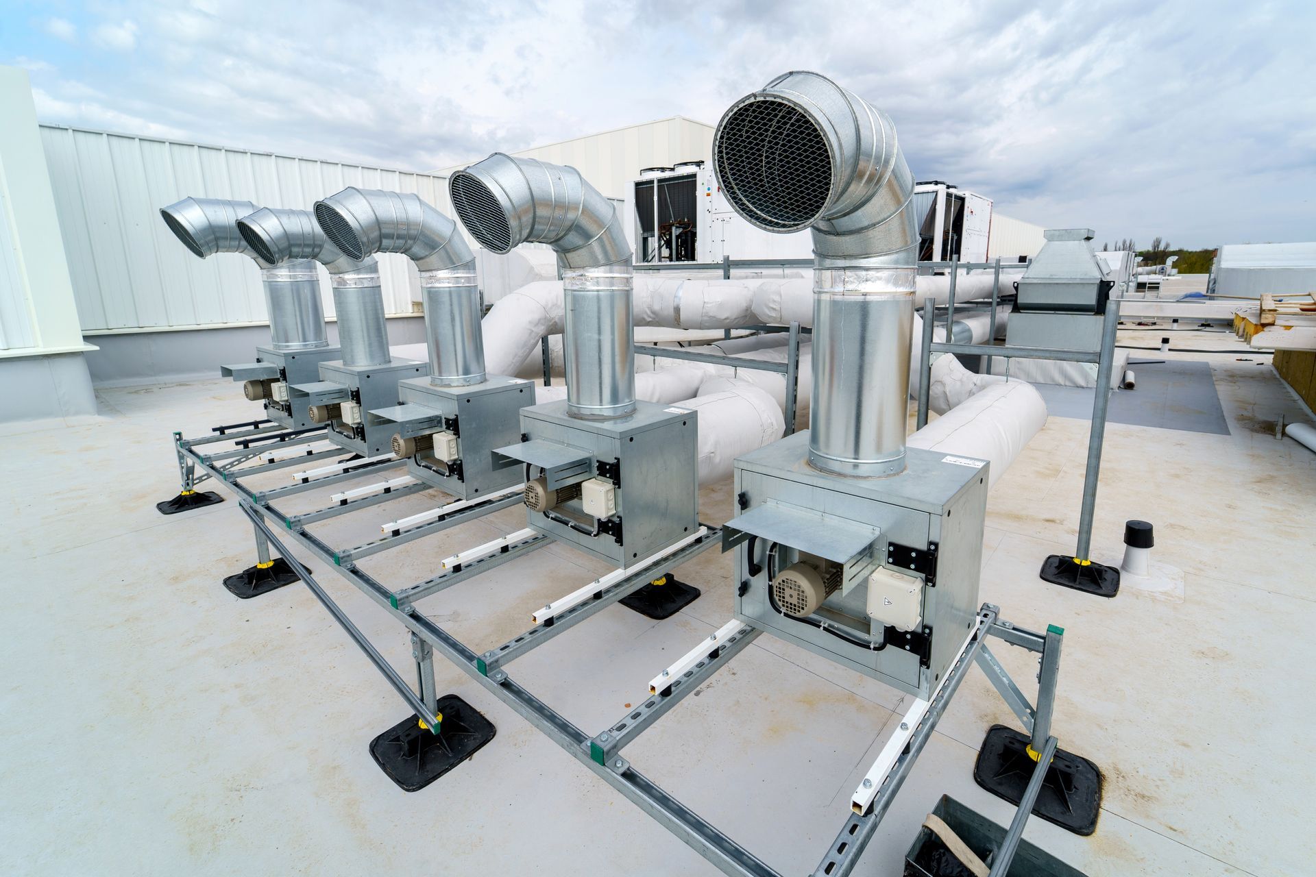 Rooftop HVAC system with silver ducts and machinery, against a cloudy sky.