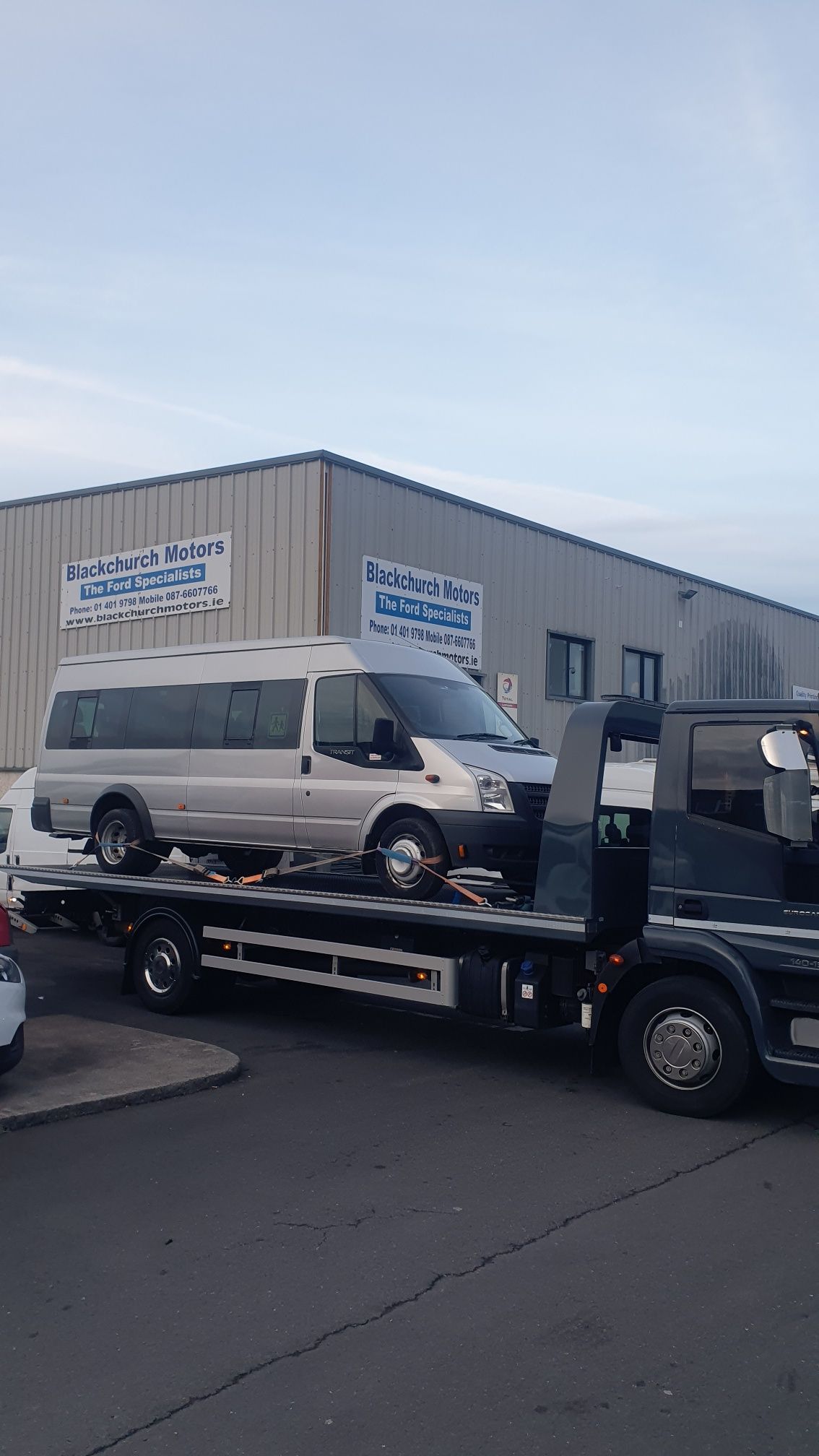 Tow truck loading a white van outside an industrial building.