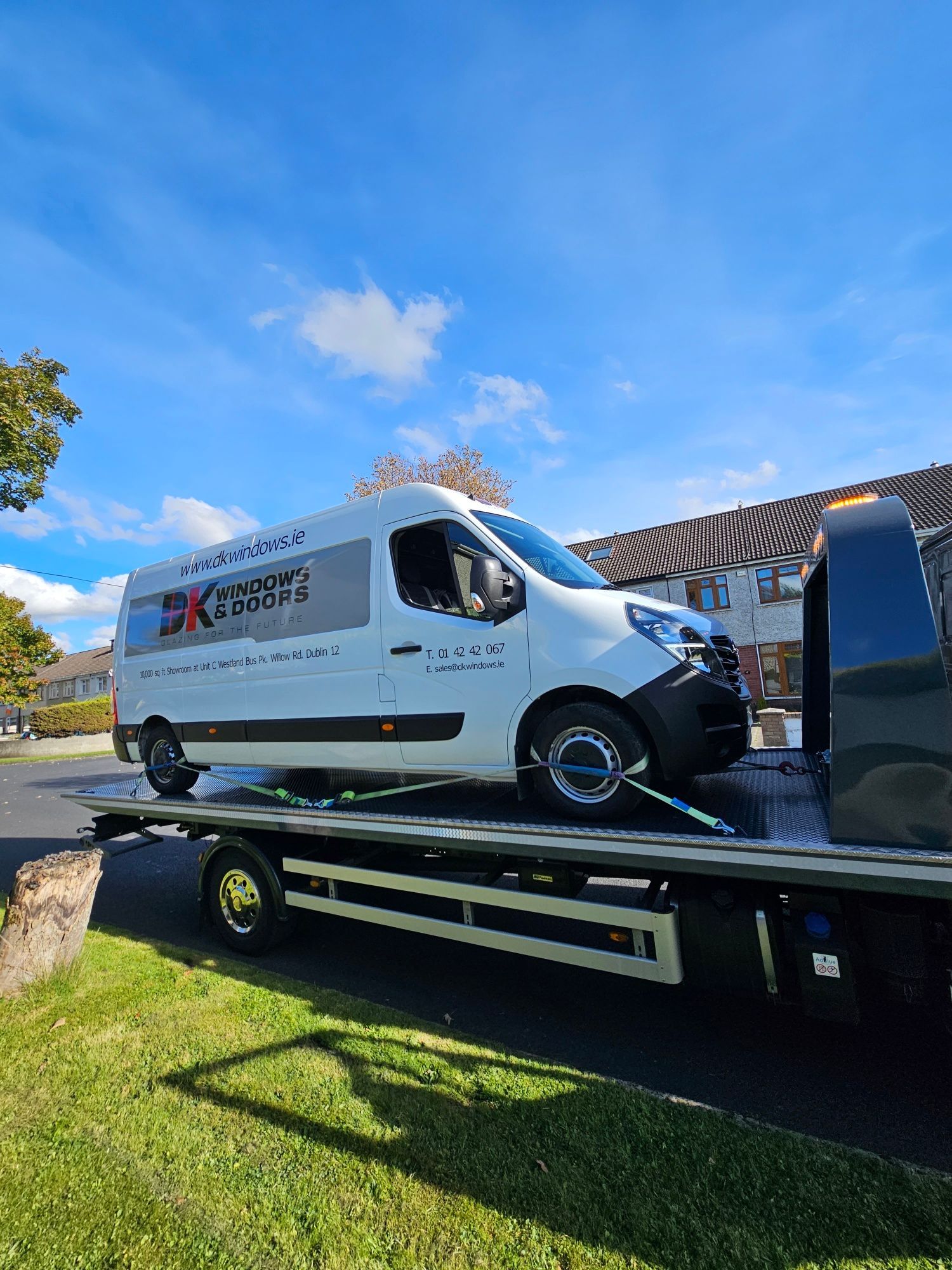 White service van on a flatbed truck under a blue sky, parked on grass outdoors