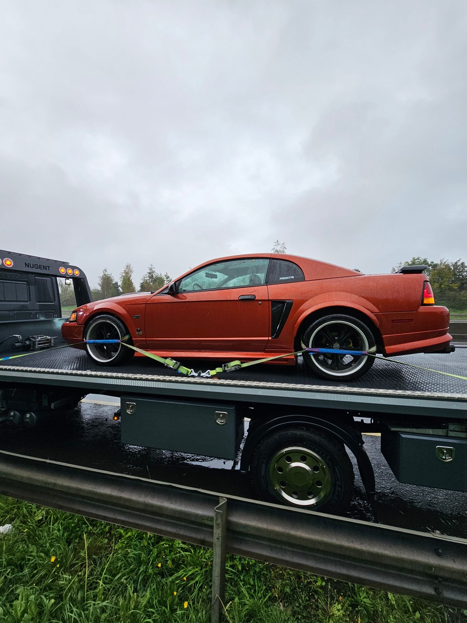 Orange custom sports car loaded on a flatbed tow truck in the rain