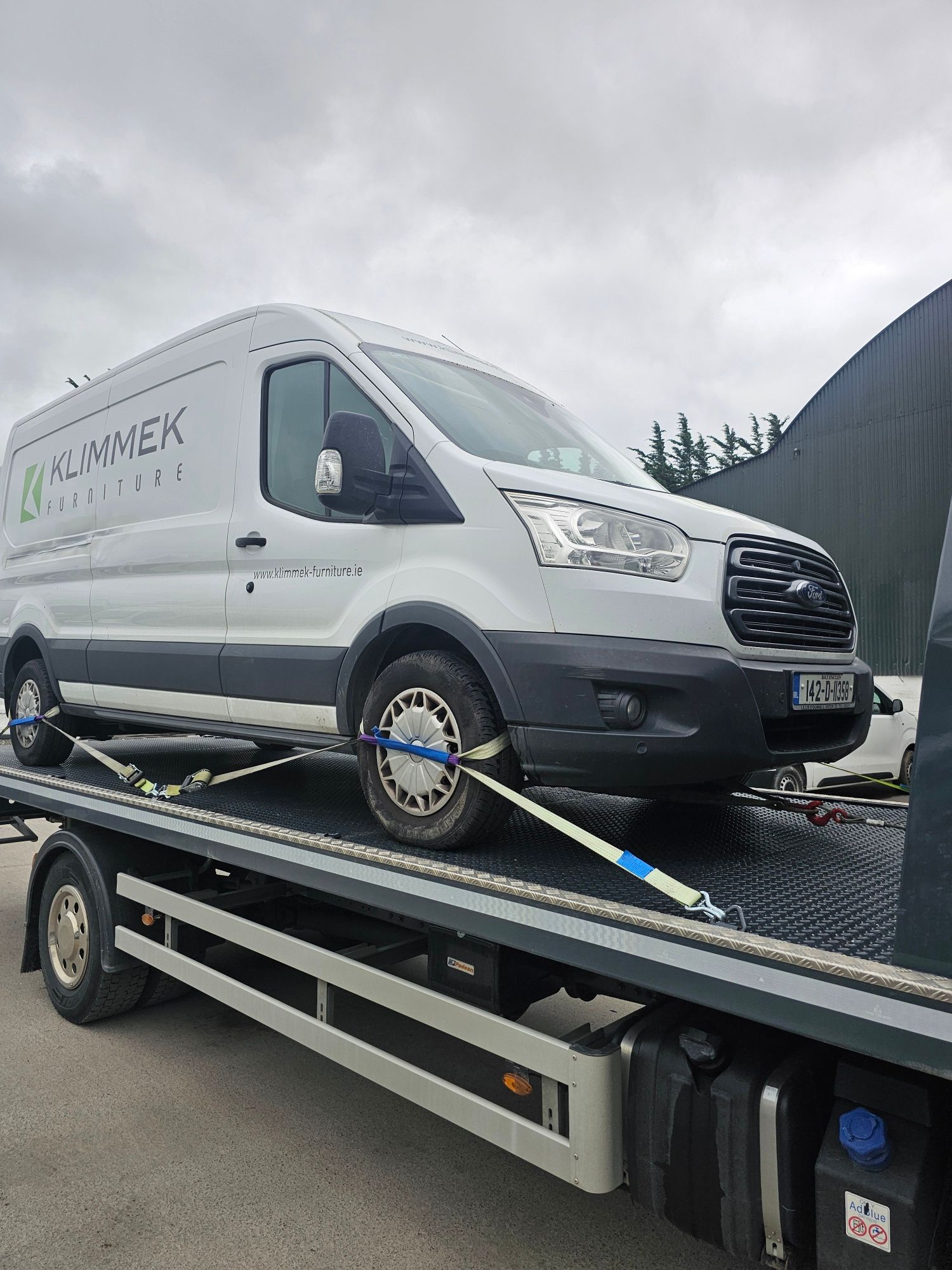 White cargo van strapped on a flatbed tow truck under a cloudy sky