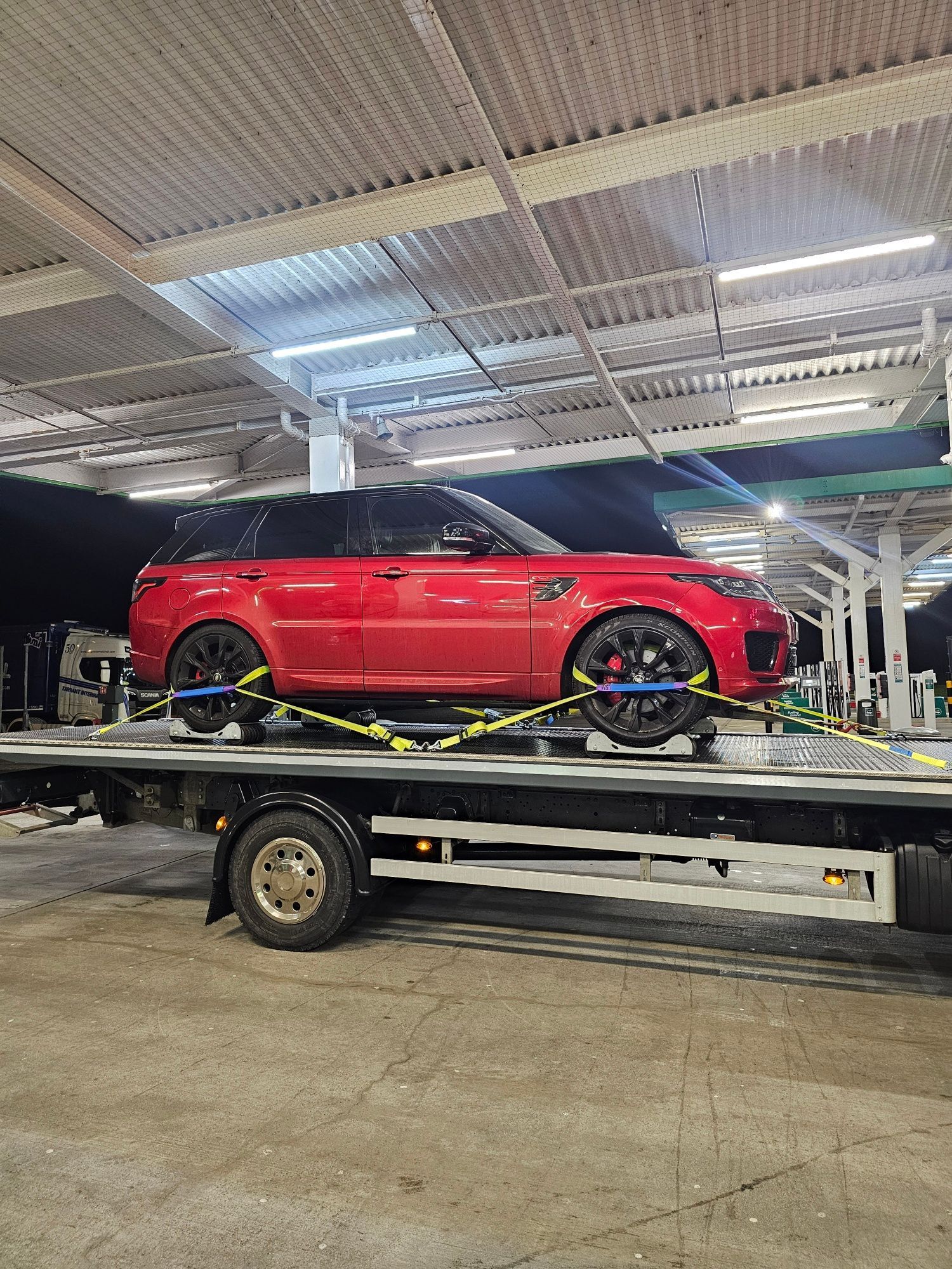 Red SUV strapped on a flatbed tow truck inside a covered parking garage.