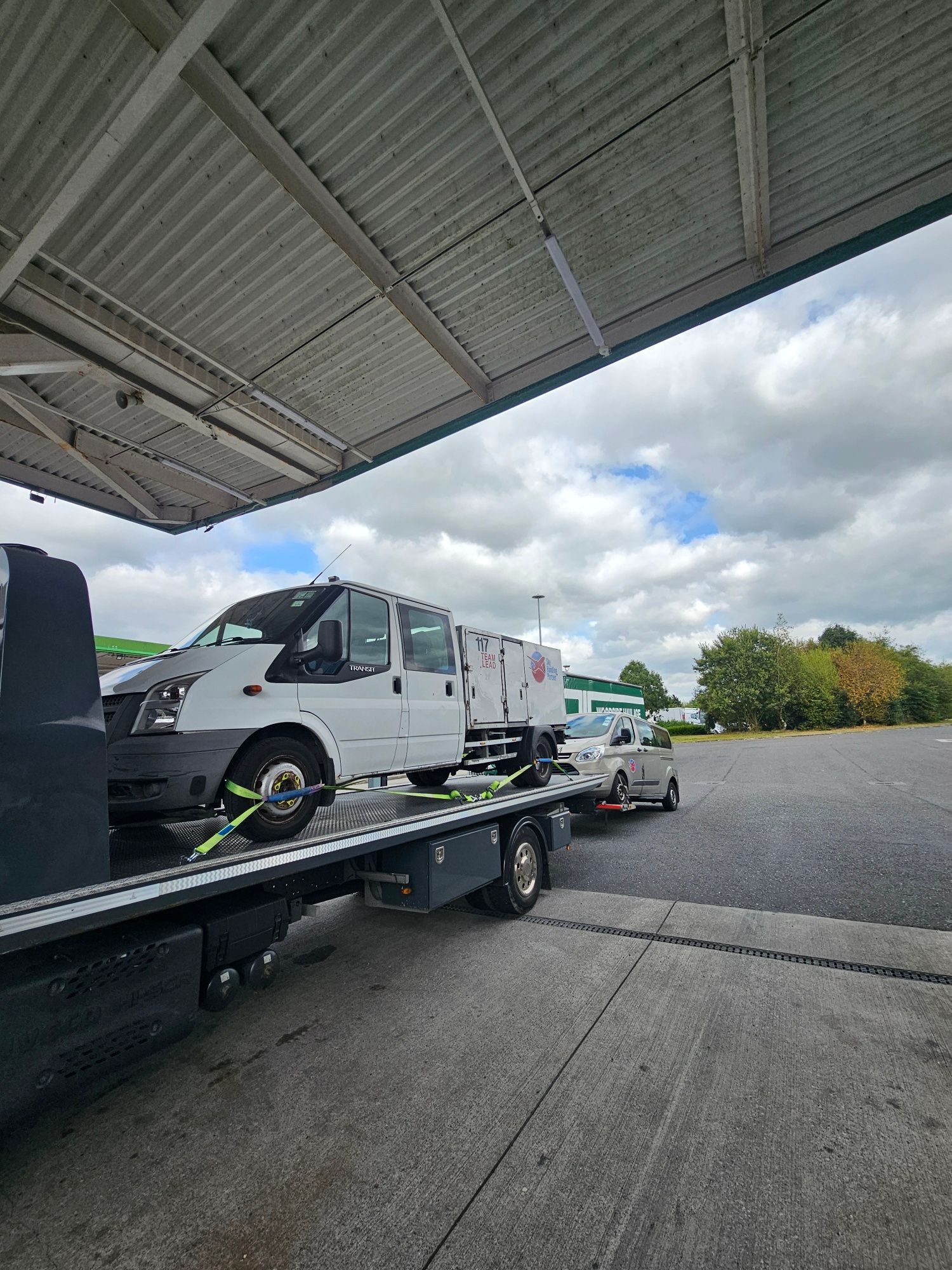 White delivery van loaded on a flatbed tow truck under a gas station canopy.