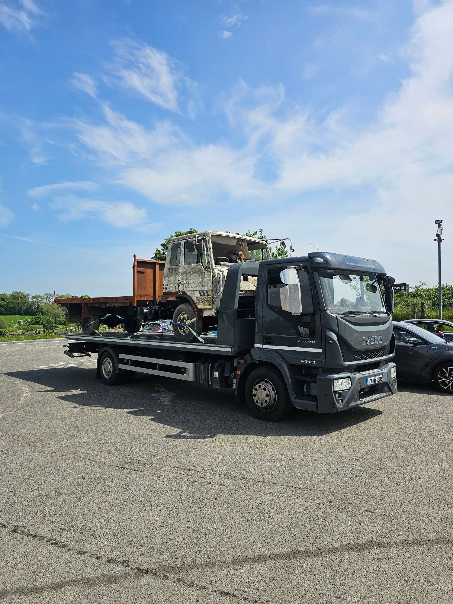 Tow truck carrying a dump trailer in a gravel lot under a blue sky