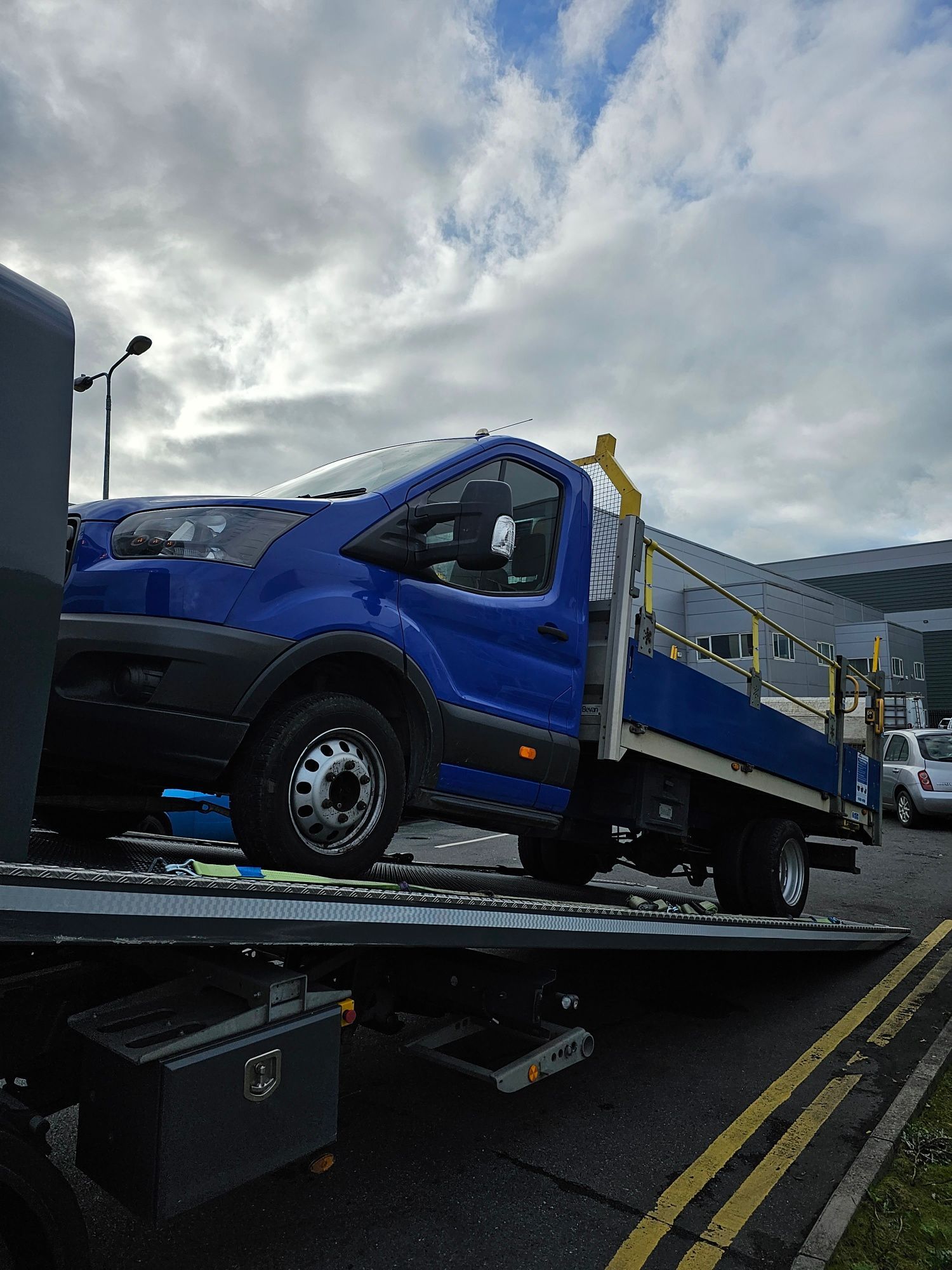 Blue flatbed truck on a tow truck ramp under a cloudy sky