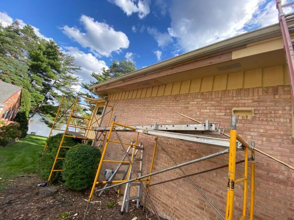 Scaffolding next to a brick building. Construction work near the roofline, against a blue sky.