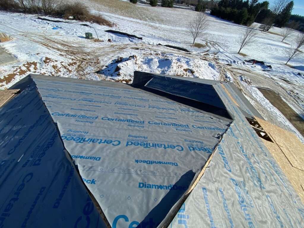 Roofing under construction covered with gray underlayment. Snowy ground in the background.