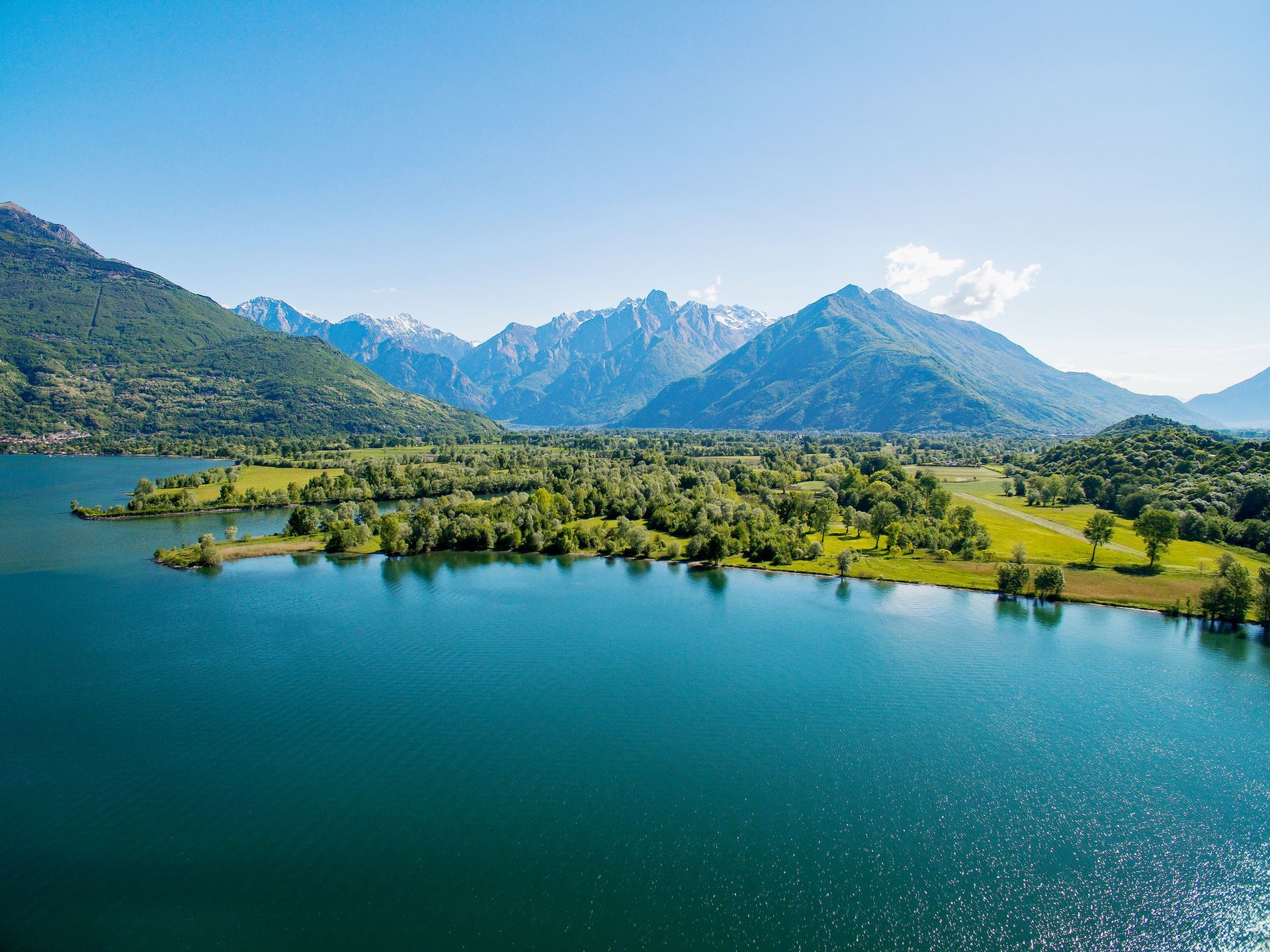 Lago blu e alberi verdi con montagne sullo sfondo sotto un cielo limpido.