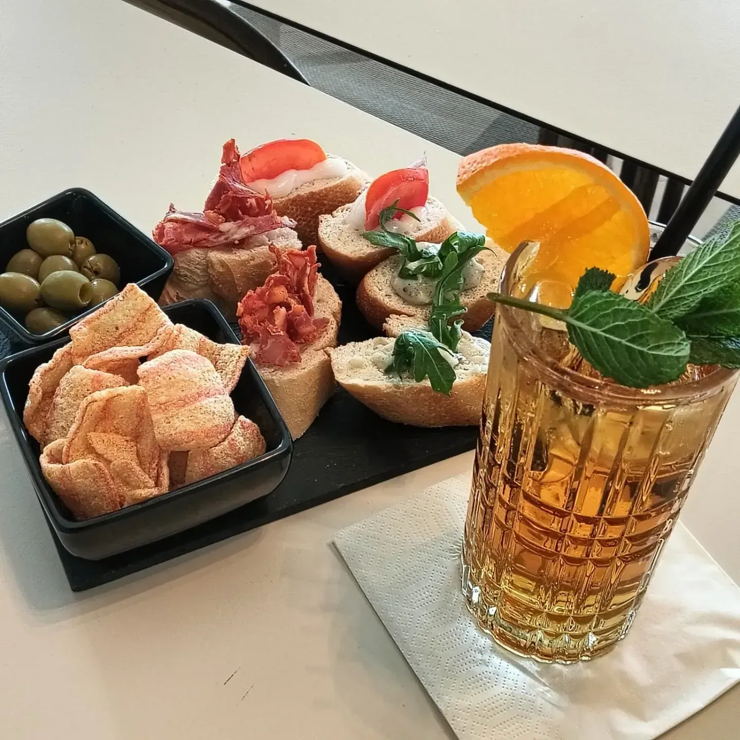 Antipasti e cocktail: olive, patatine, bruschetta e una fetta d'arancia con menta.