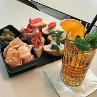 Antipasti e cocktail: pane, olive, patatine e una bevanda con guarnizione di arancia e menta.