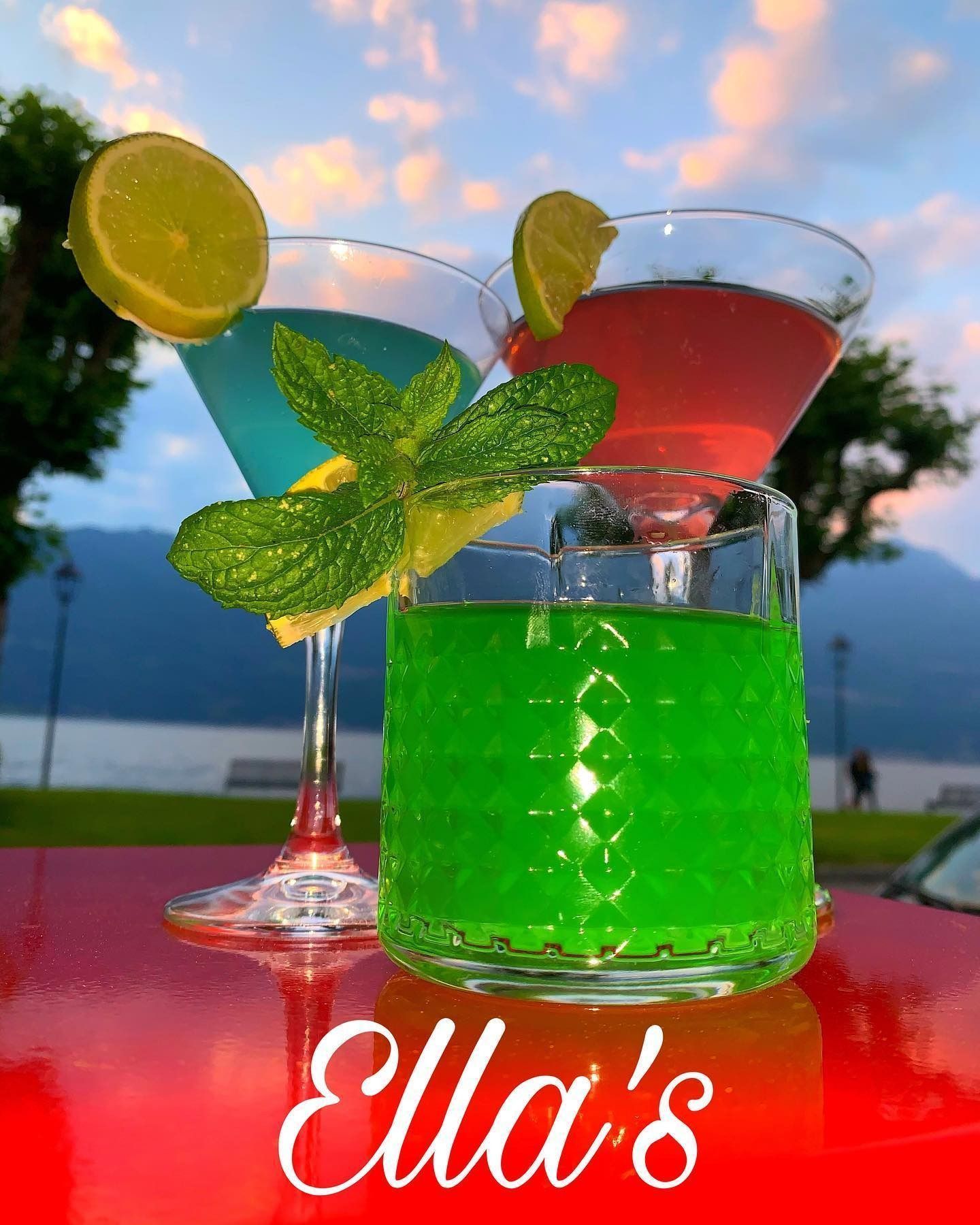 Cocktail: blu, verde e rosso in bicchieri con guarnizione di lime e menta, su una superficie rossa, sfondo scenico.