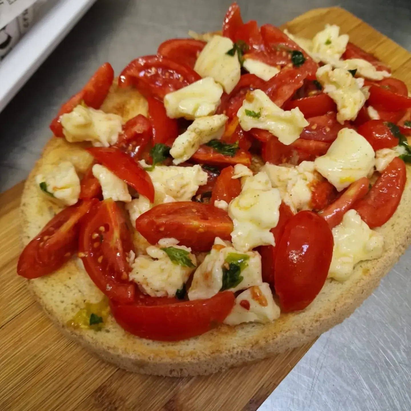 Pane piatto condito con fette di pomodori rossi, mozzarella ed erbe aromatiche.