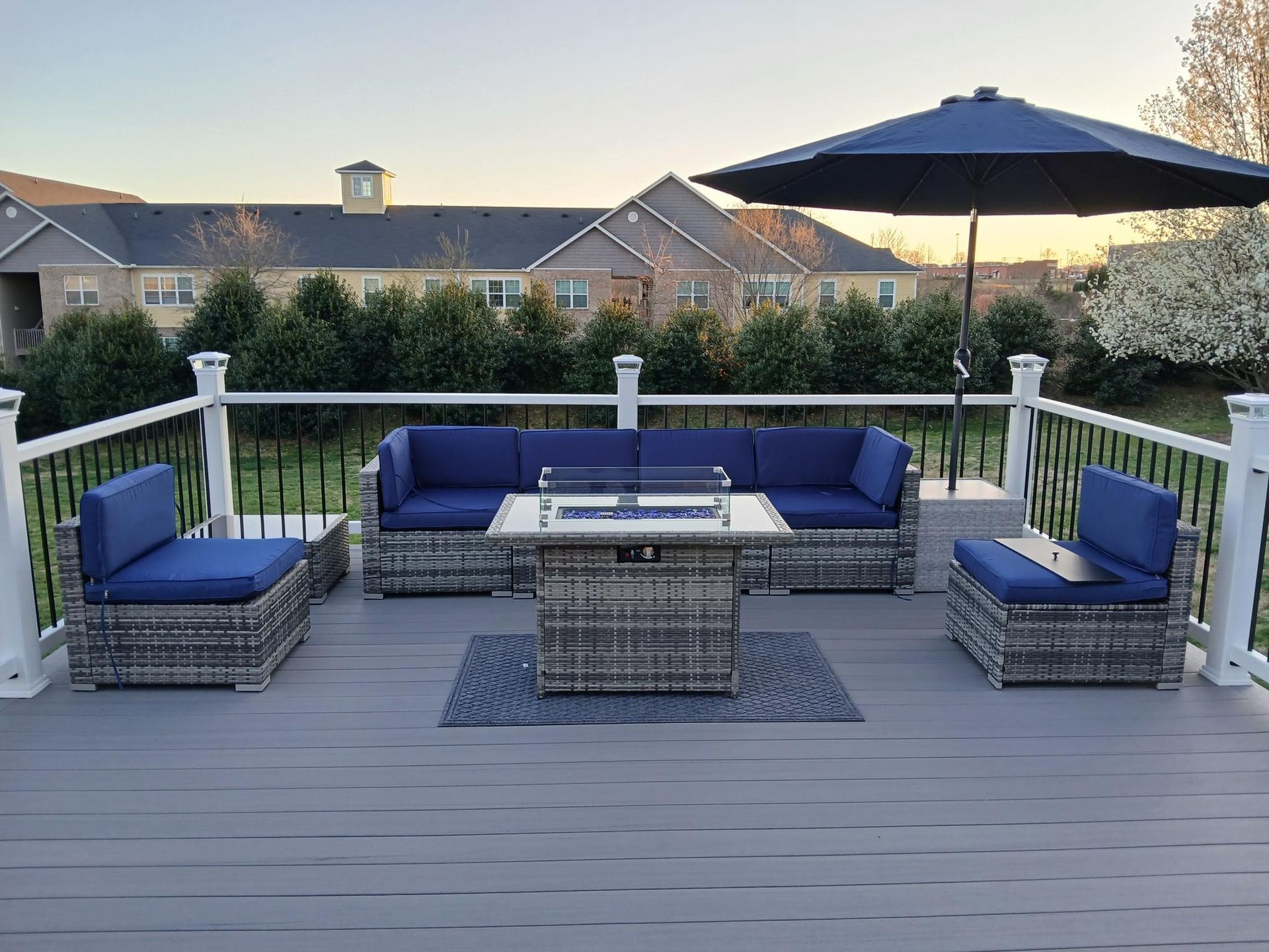A deck with a fire pit , couch , chairs and umbrella.
