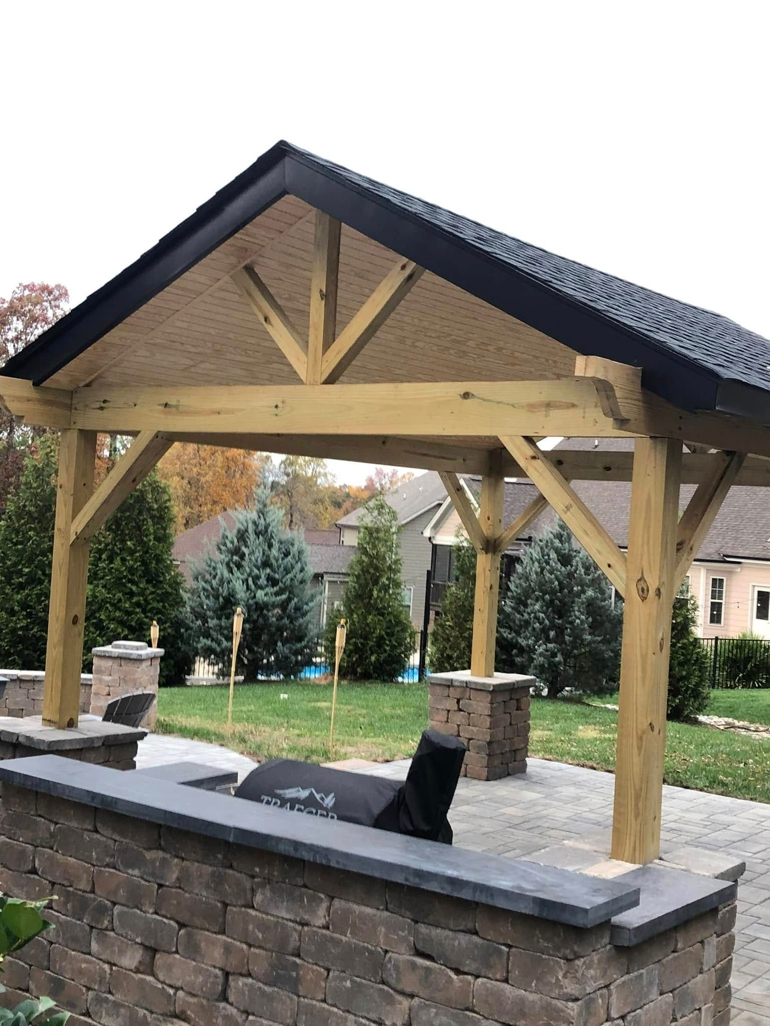 A wooden gazebo with a black roof is sitting on top of a brick wall.