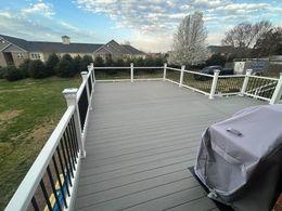 A gray deck with a white railing and a grill on it.