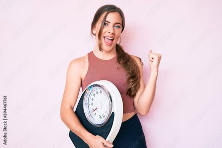 A young woman is holding a scale and making a funny face.