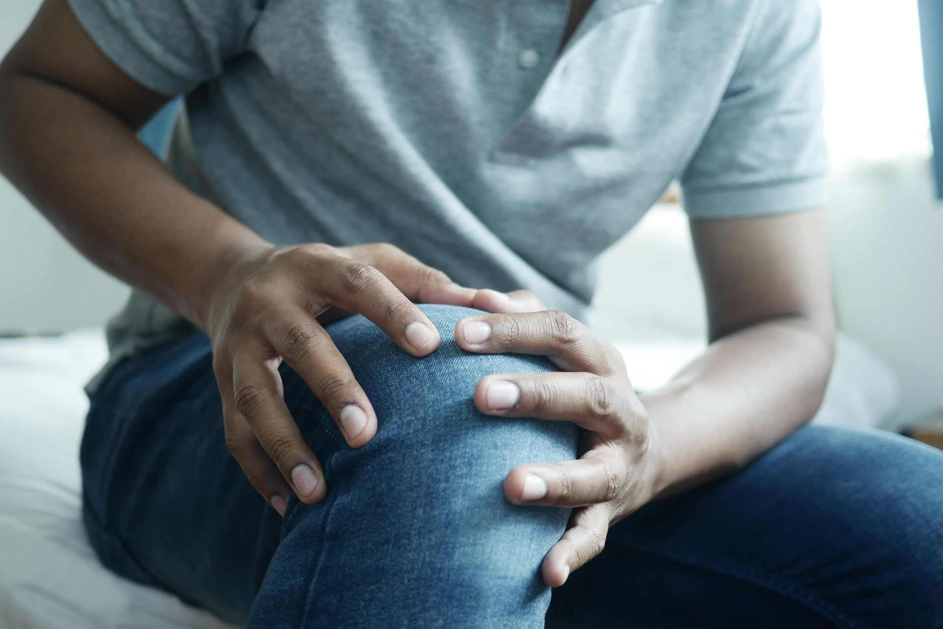 A man is sitting on a bed holding his knee in pain.