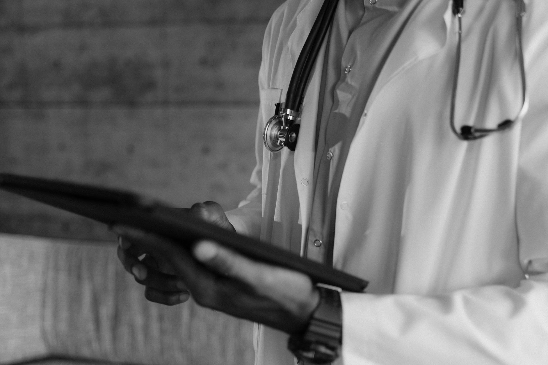 A doctor with a stethoscope around his neck is holding a tablet.