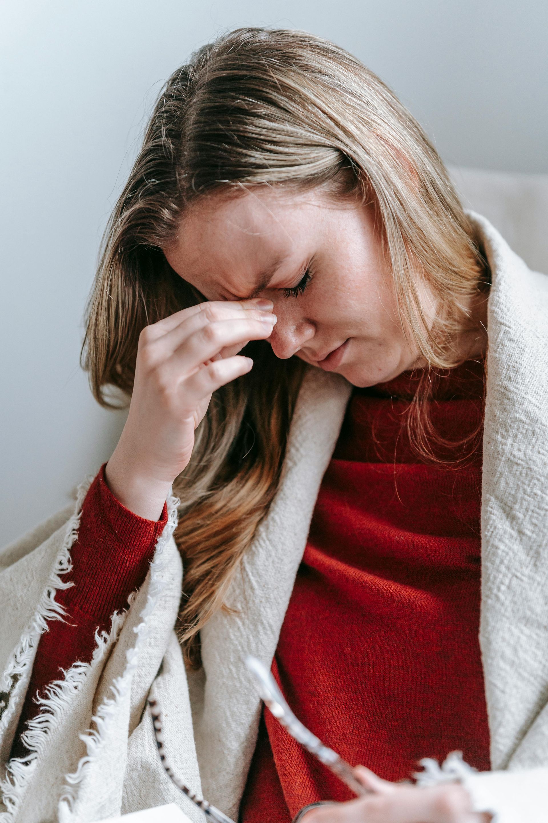 A woman wrapped in a blanket is sitting in a chair with a thermometer in her hand.