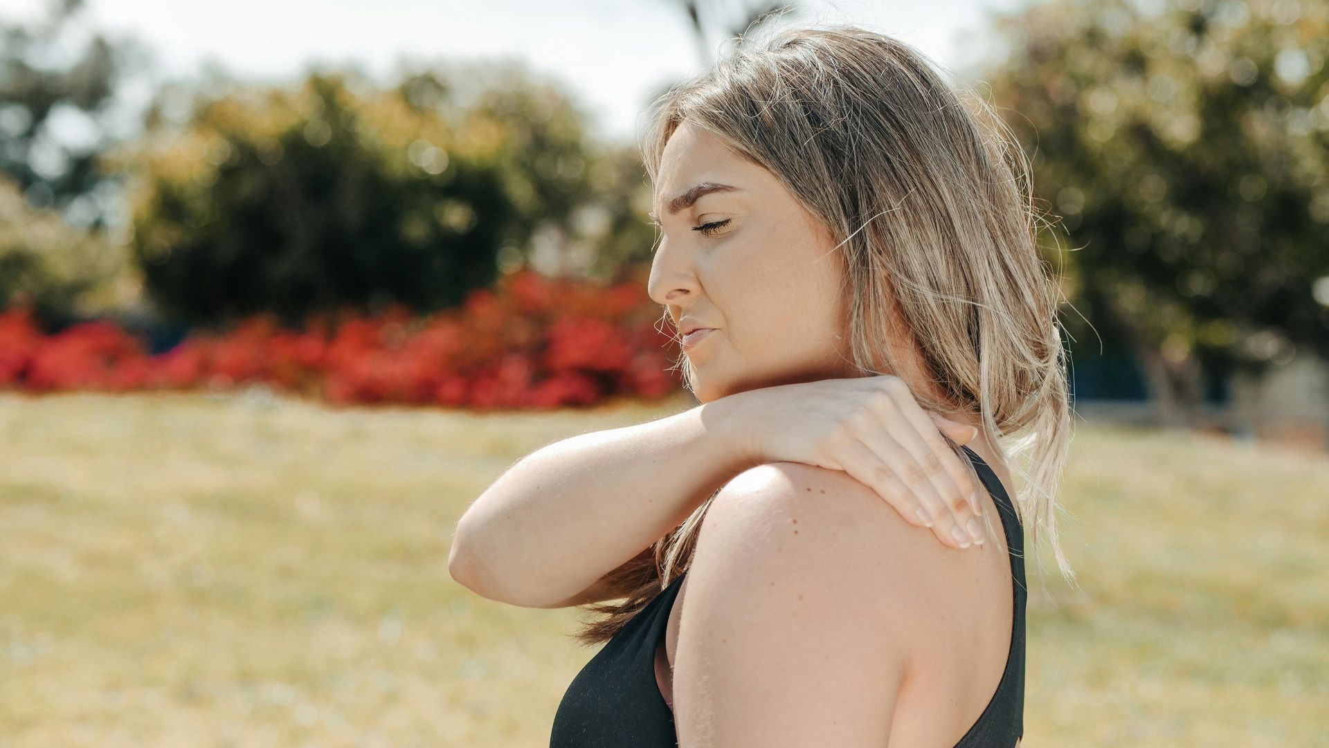 A woman is holding her shoulder in pain while standing in a field.