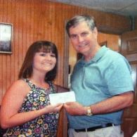 Woman in floral top receiving a check from a man in a blue shirt. Interior setting.