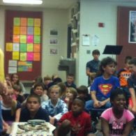 Classroom of children watching a presentation; a few children are wearing superhero shirts.