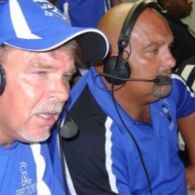 Two men wearing blue shirts and headsets, focused intently.
