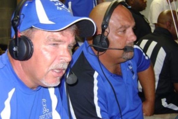 Two men wearing blue headsets and shirts, possibly coaches, looking intently.