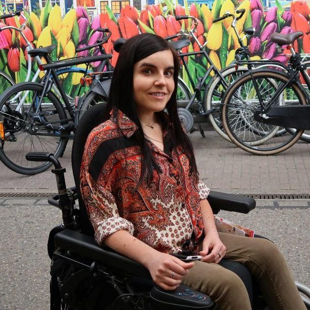 a woman in a wheelchair is smiling in front of a wall of flowers