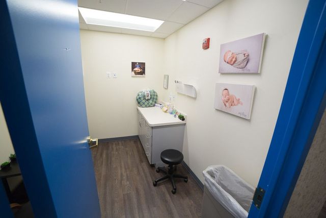 A doctor's examination room with light blue door frame. Room features a cabinet, stool, and baby-themed artwork.