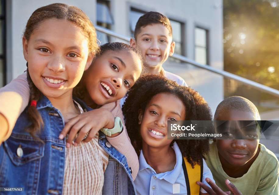 Group of five diverse children smiling outdoors, some with arms around each other.