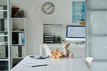 Bright, airy office with a desk holding a teddy bear and wooden toy. Shelves in the background.