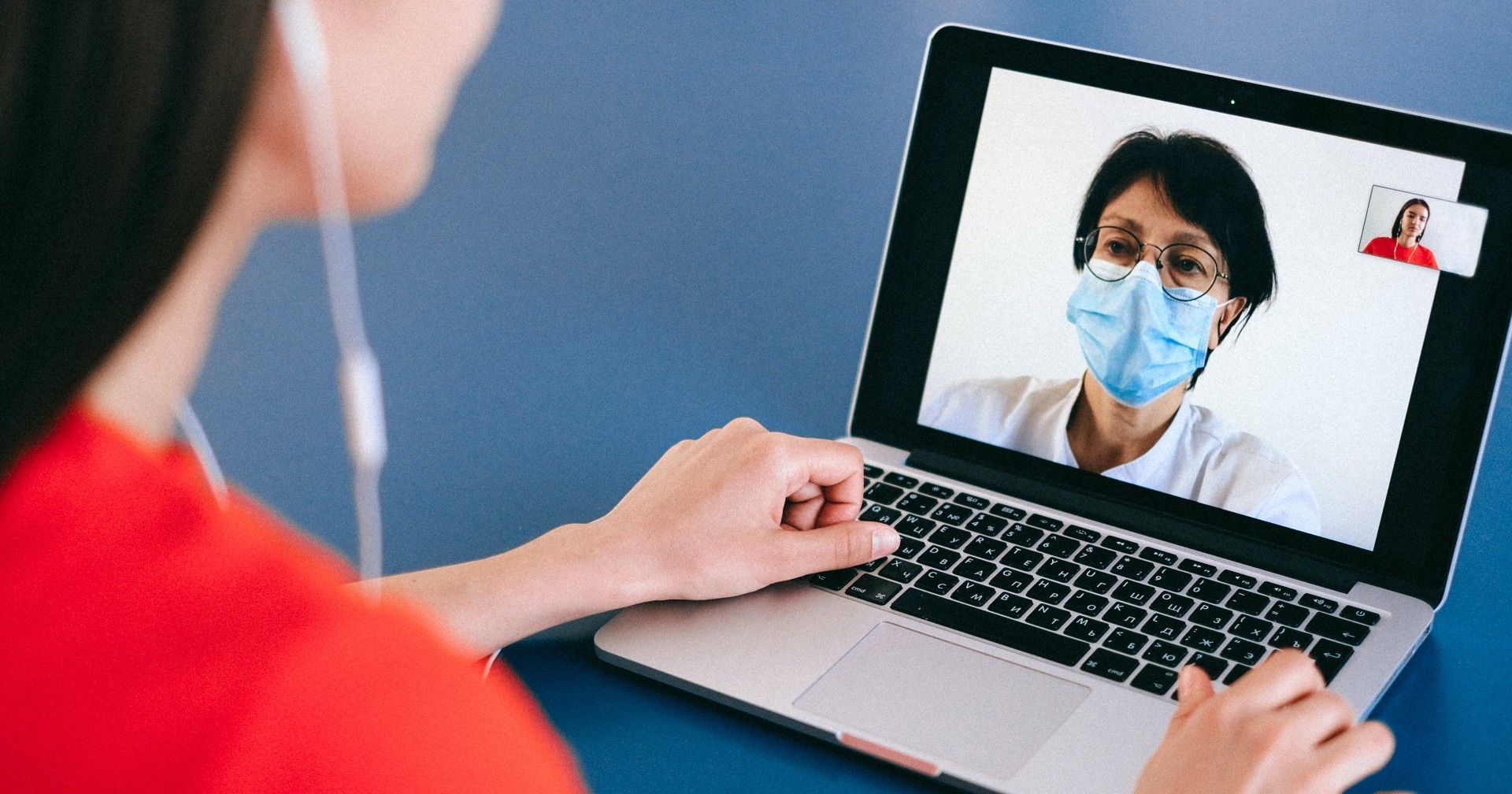A woman wearing a mask is having a video call with a doctor on her laptop.