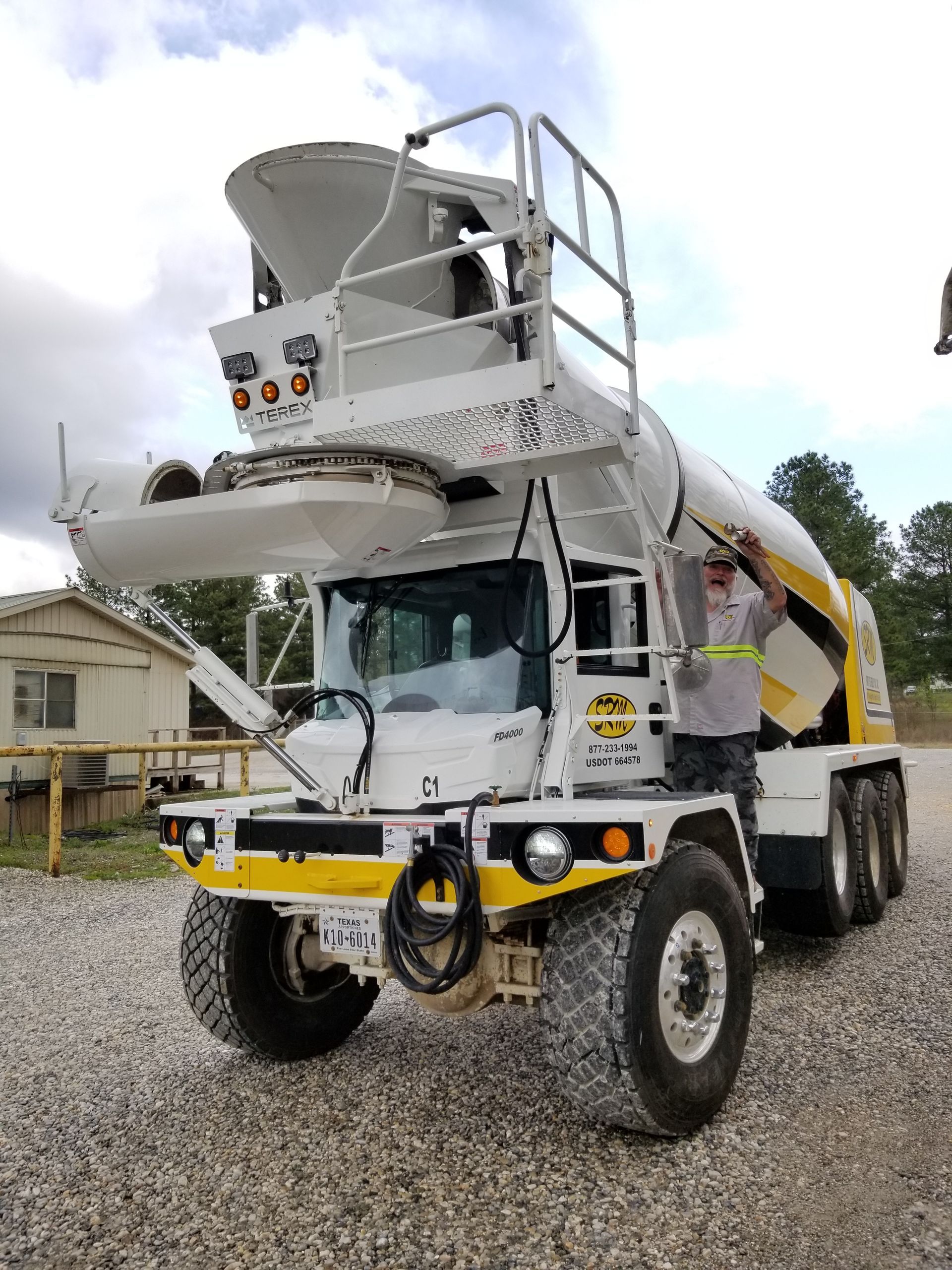 White and yellow concrete mixer truck with a worker standing next to it.