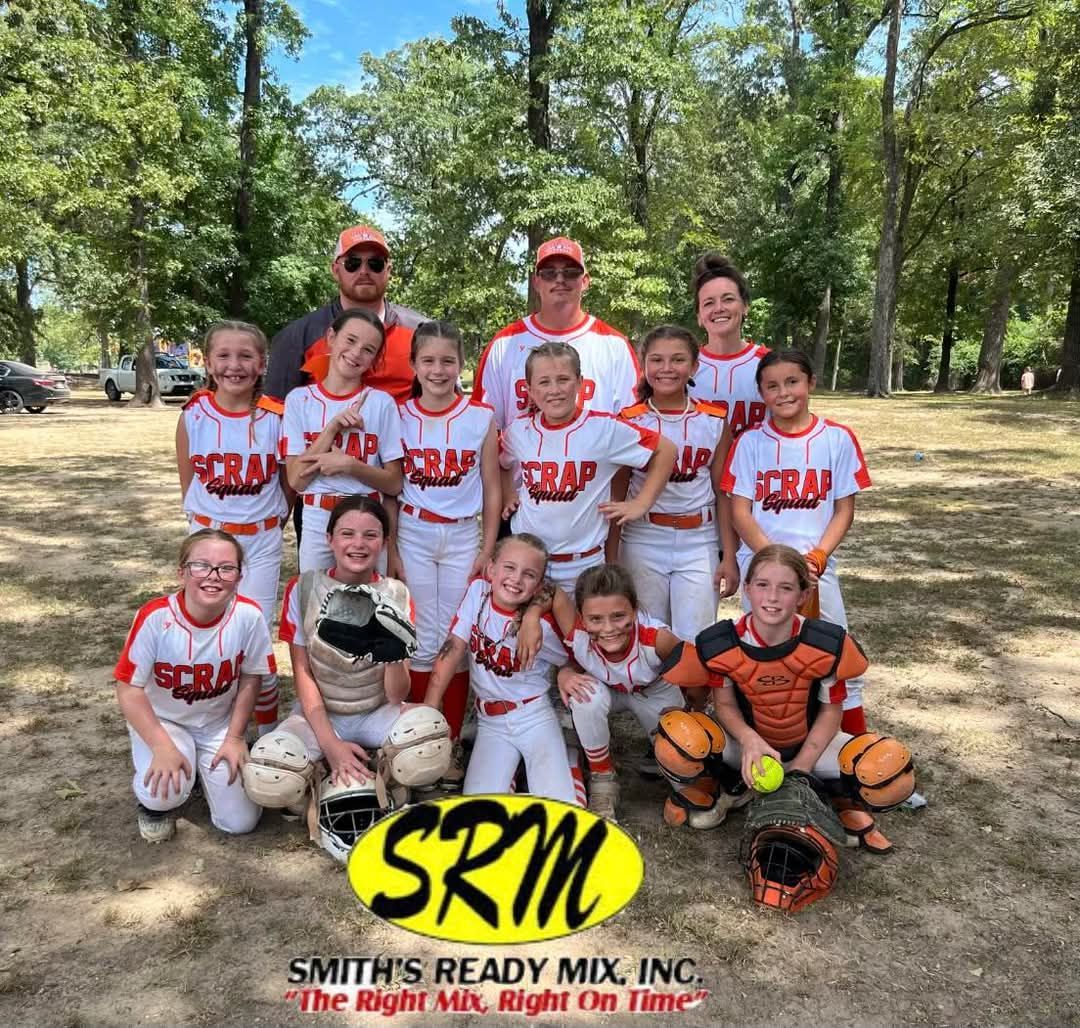 Youth softball team in white/orange uniforms, posing with coaches on a sunny field. SRM logo at the bottom.