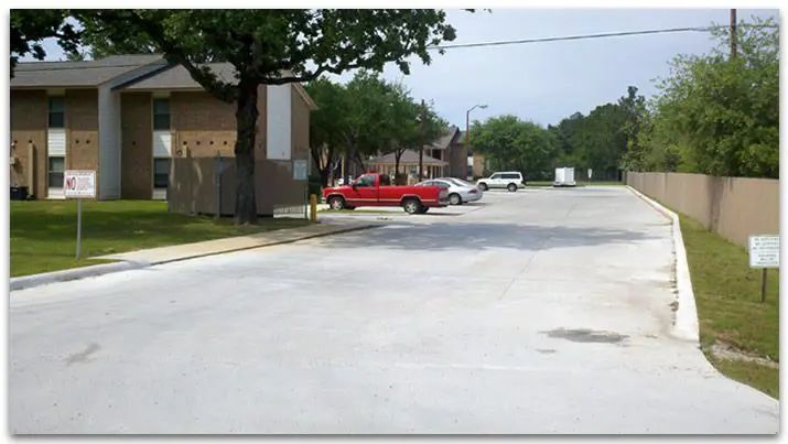 Parking lot with red truck and two other cars parked. Apartment buildings on the left, tan wall on right.