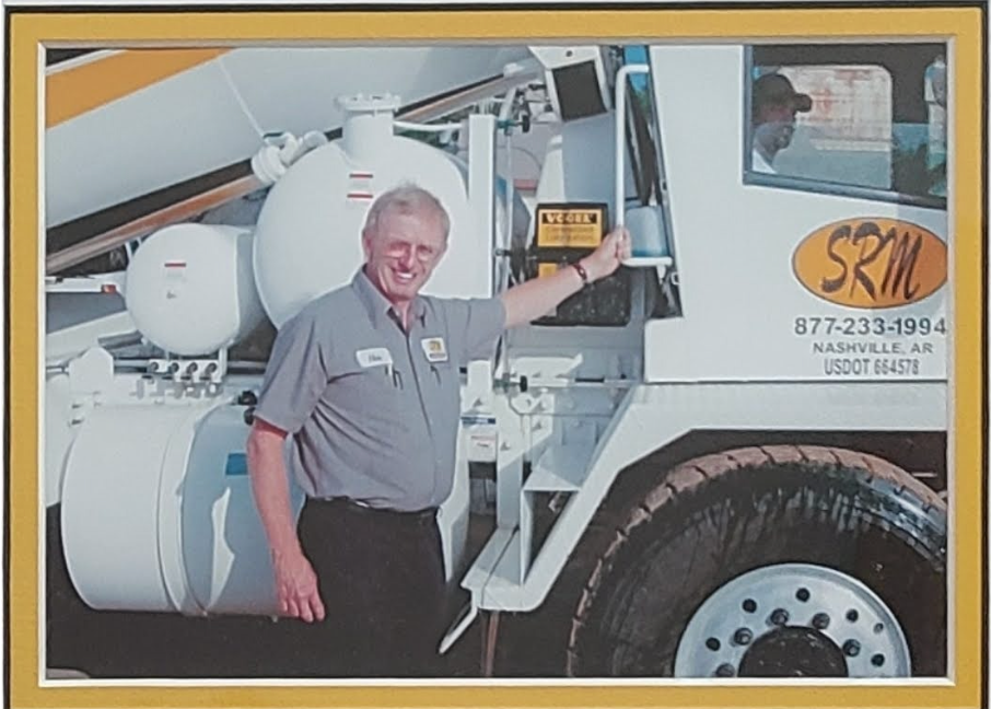 Man in uniform standing next to a white SRM concrete truck, smiling. Nashville, AR address.