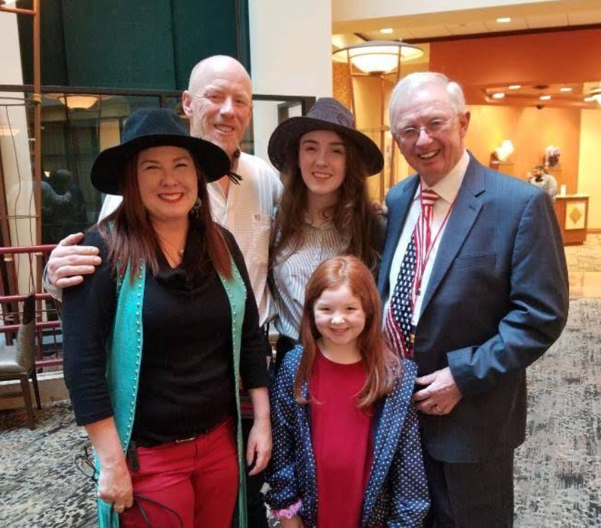 Family of five smiling for a photo in an interior setting; some wear hats.