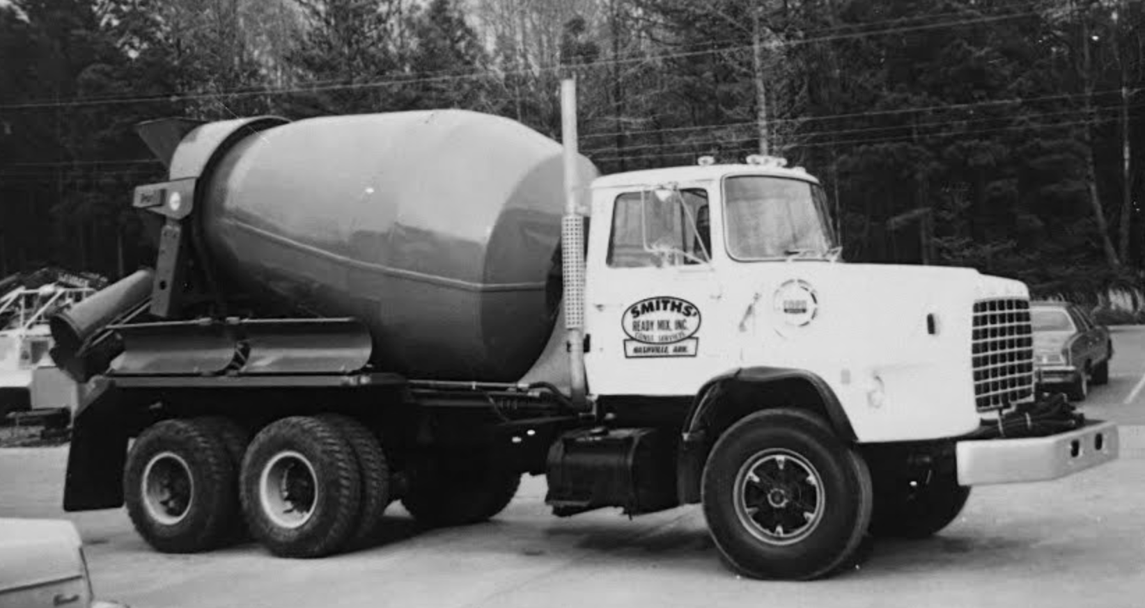 Black and white photo of a white concrete mixer truck with a large rotating drum, parked outside.