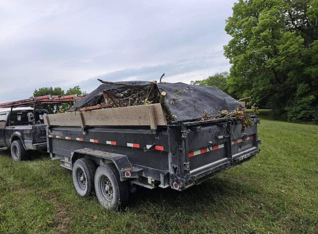 A dump truck is pulling a trailer full of trash in a grassy field.