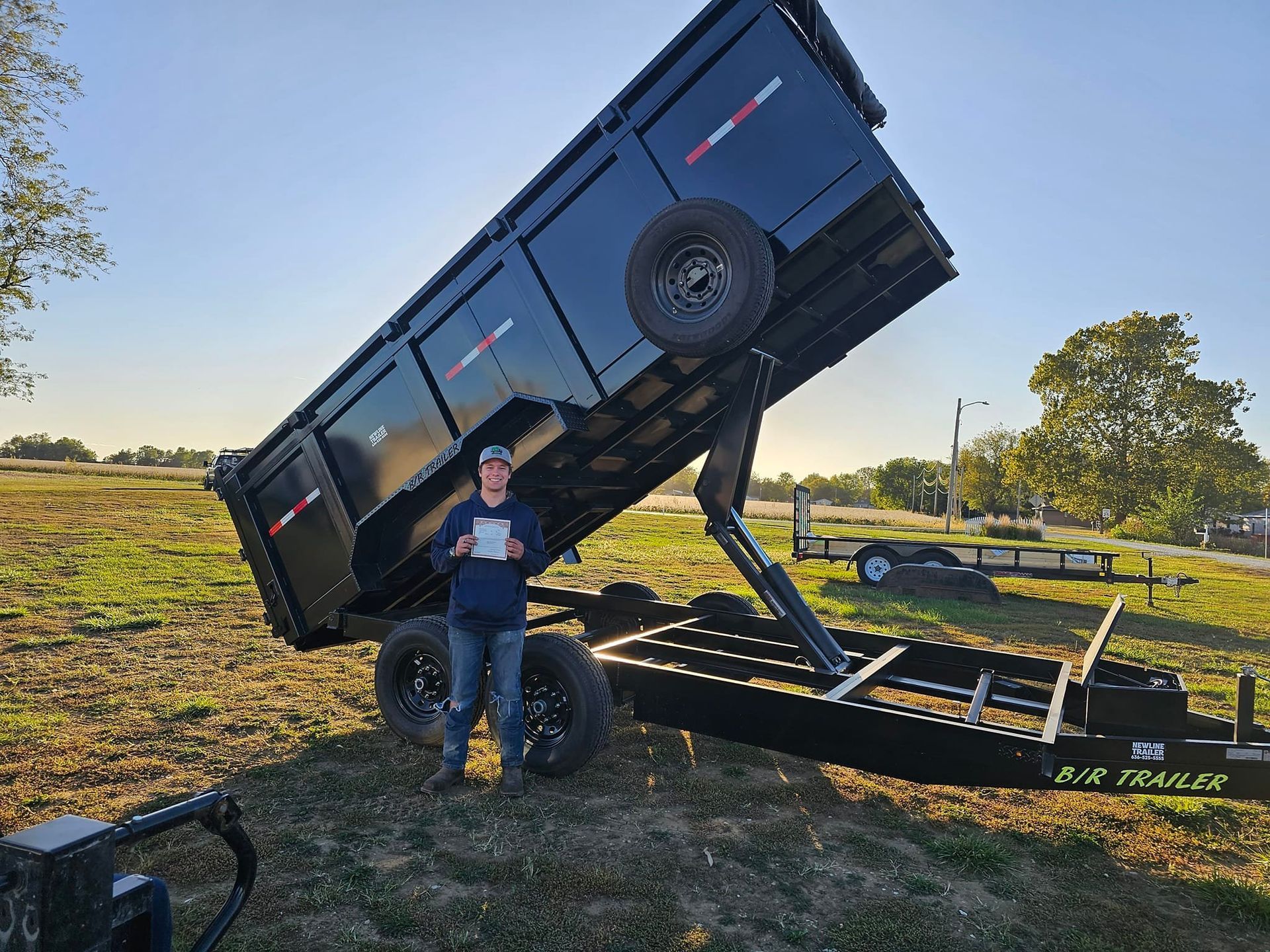 A man is standing next to a dump trailer in a field.