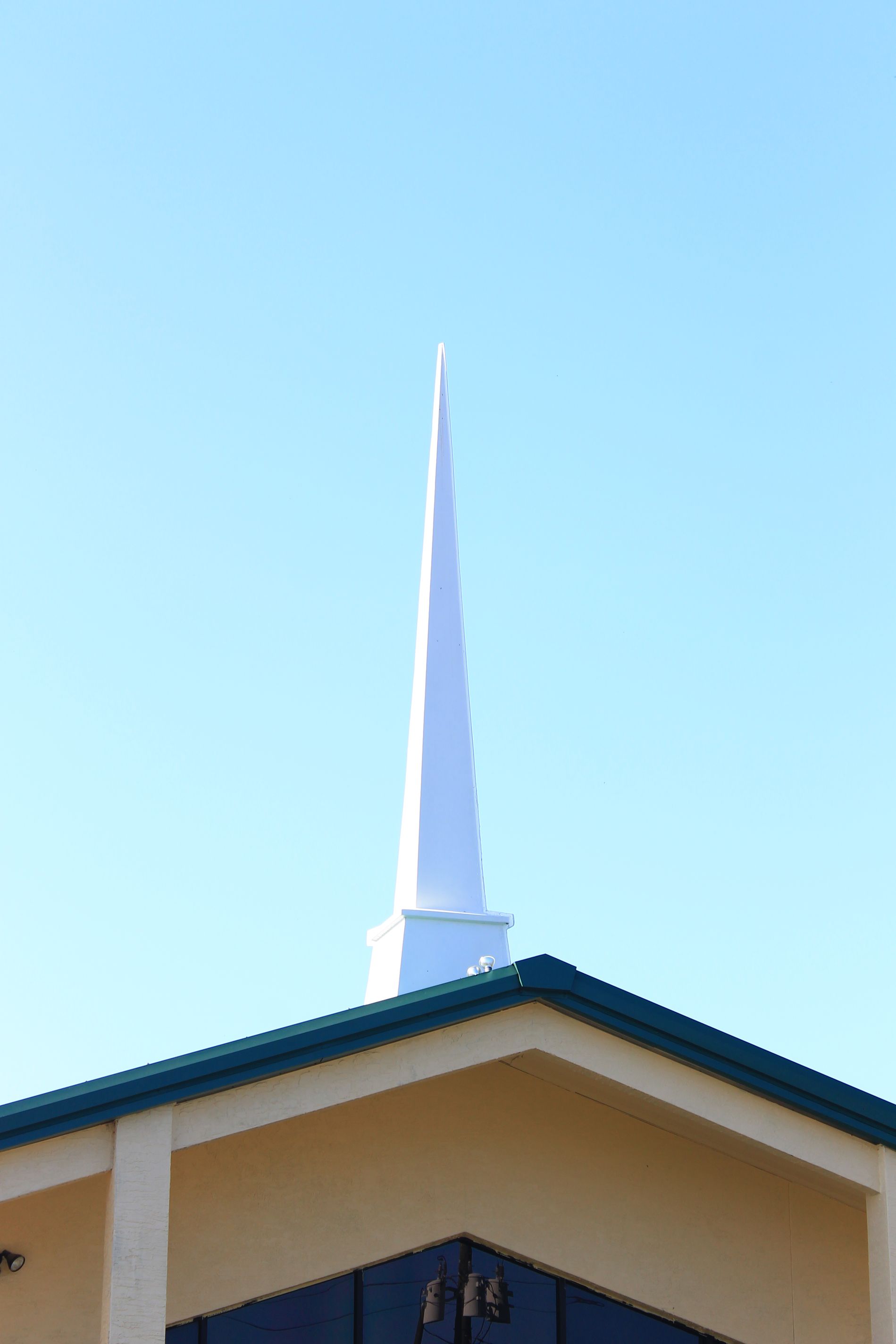 White church steeple atop a tan building with a blue sky.