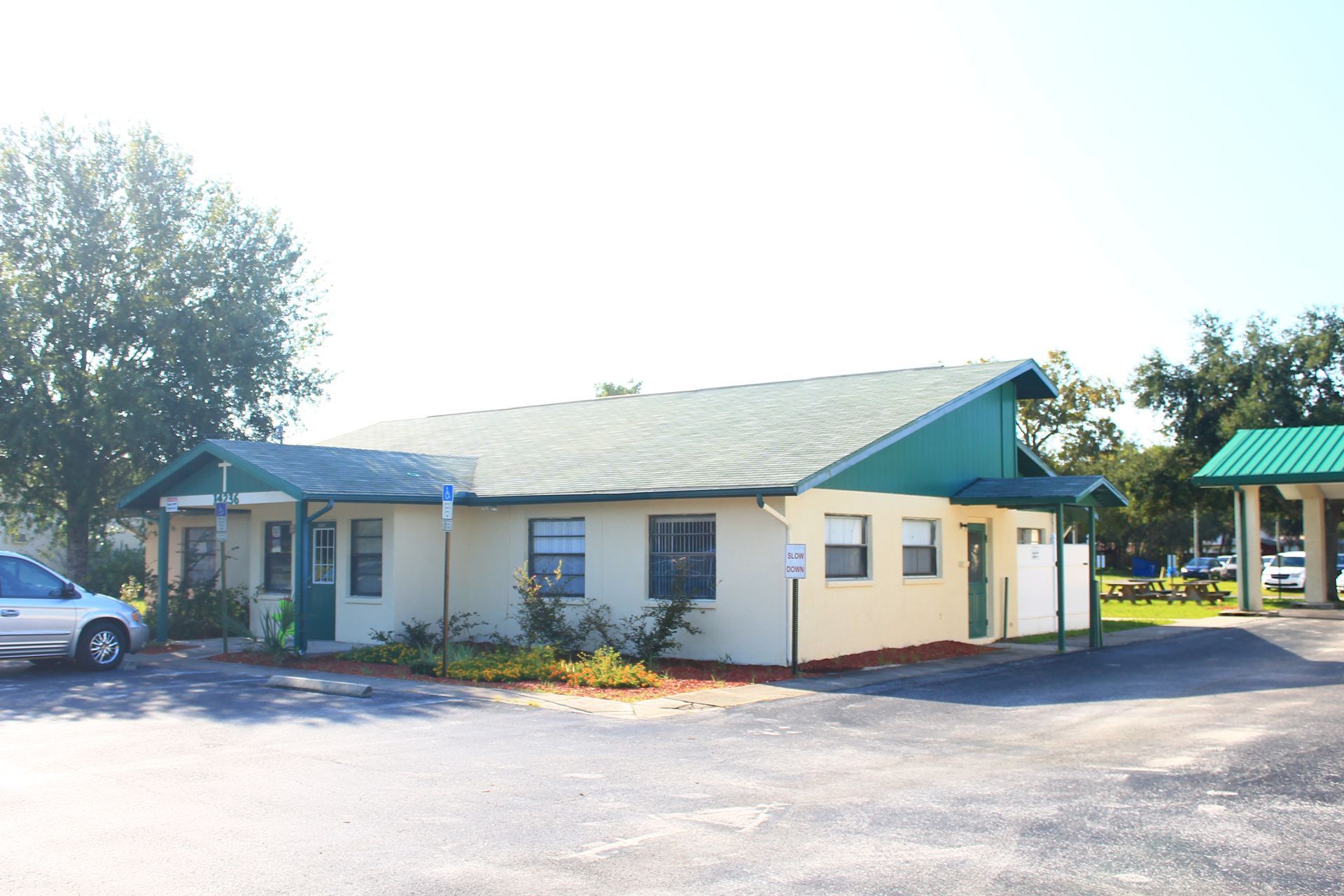 Exterior view of a light beige building with a green roof and accents. Sunlight shines.