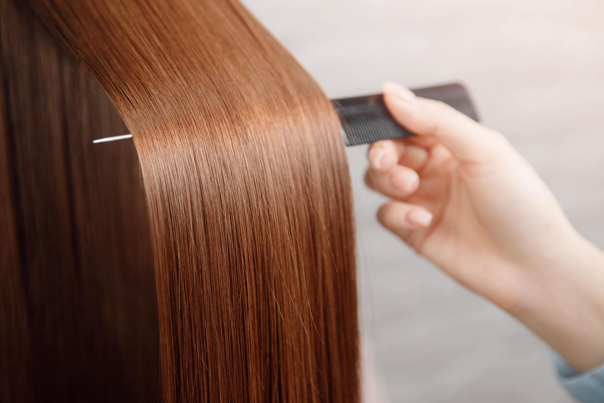 Person combing glossy, straight, brown hair with a black comb.