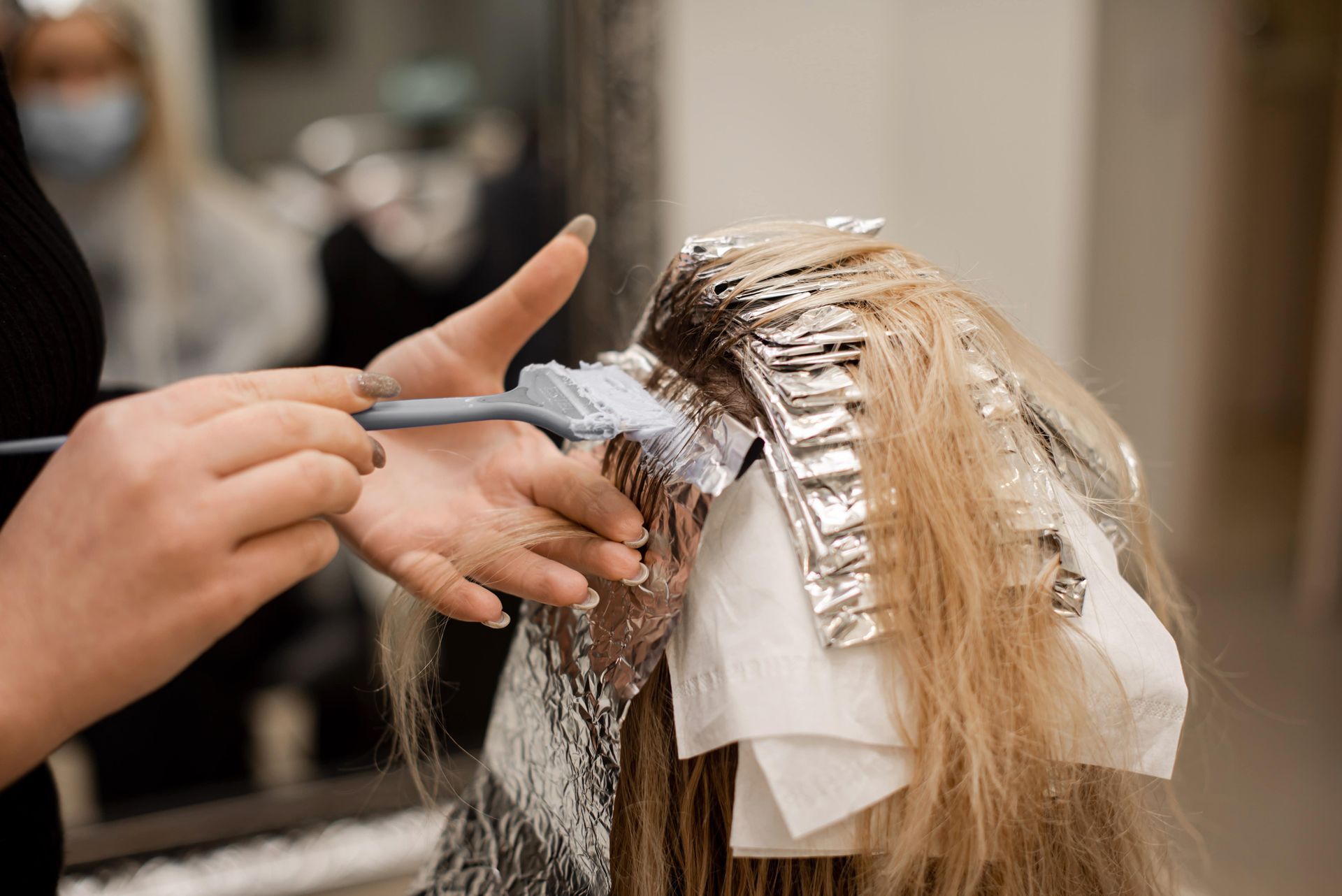 Hairdresser applying dye to blonde hair with foil highlights in a salon.